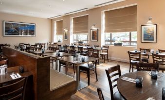 a large dining room with wooden tables and chairs , several windows , and paintings on the wall at DoubleTree by Hilton Swindon