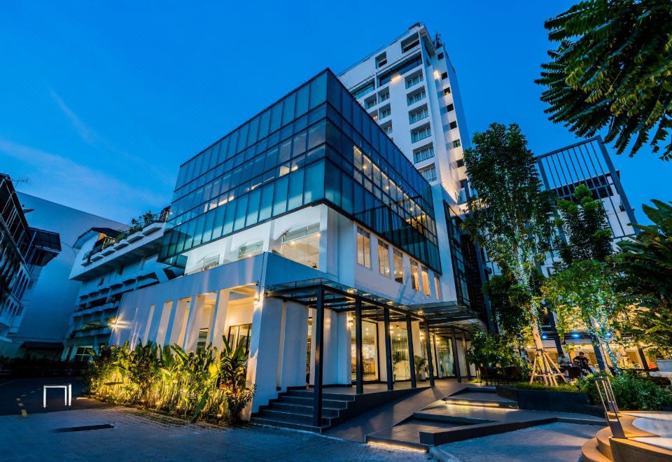 a modern building with a glass facade and white walls , surrounded by trees and other buildings at night at Rattanachol Hotel
