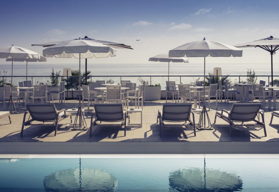 a group of umbrellas and chairs on a rooftop lounge area , with a pool visible in the background at Mercure Villeneuve Loubet Plage