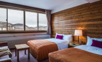 a hotel room with two beds , one on each side of the room , and a view of mountains outside the window at Okushiga Kogen Hotel