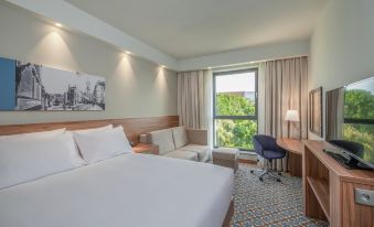 a modern hotel room with a large window , white bed , and desk , along with a couch and bed at Hampton by Hilton Oswiecim