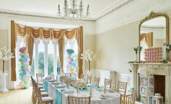 a formal dining room with a long table set for a party , adorned with balloons and centerpieces at Delta Hotels Breadsall Priory Country Club