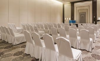 In a spacious conference room, rows of white chairs are arranged facing the front, creating an ideal setting for events or gatherings at Graph Hotels