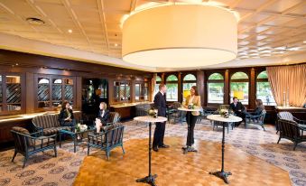 a dining room with people sitting at tables , serving drinks and food , surrounded by elegant decor and large windows at Maritim Hotel Darmstadt