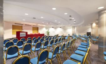 a large conference room with rows of blue and gold chairs arranged in a semicircle at B&B Hotel Trapani Crystal