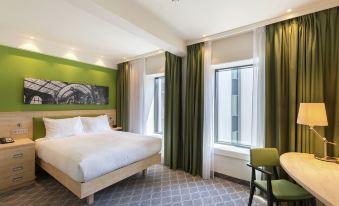a modern hotel room with a large bed , green curtains , and a window looking out to the city at Hampton by Hilton Antwerp Central Station