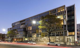 a modern apartment building with multiple balconies and large windows , surrounded by trees and lit up at night at IStay Precinct Adelaide