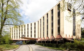 a large hotel building with multiple floors , surrounded by trees and a road , under a clear blue sky at NH Luxembourg