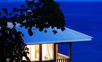 a small wooden house with a balcony overlooking the ocean , illuminated by lights at night at Antulang Beach Resort