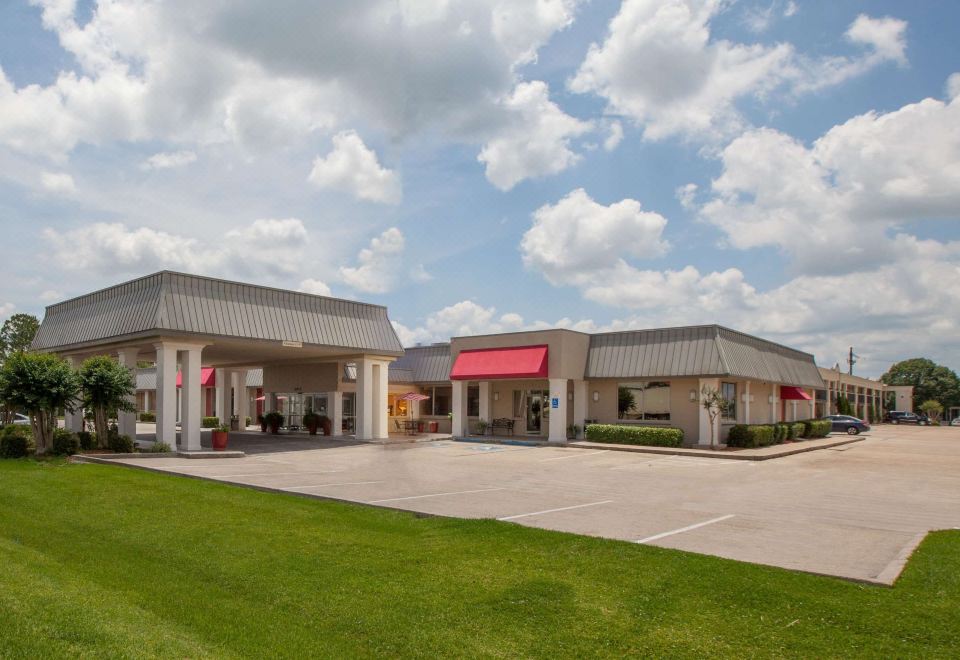 a large building with a red awning is surrounded by a green lawn and trees at Ramada by Wyndham New Iberia