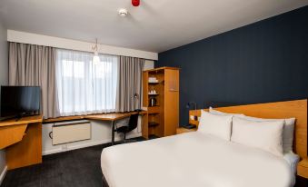 a modern hotel room with a white bed , blue walls , and a desk area equipped with a computer and other items at Holiday Inn Express Droitwich Spa