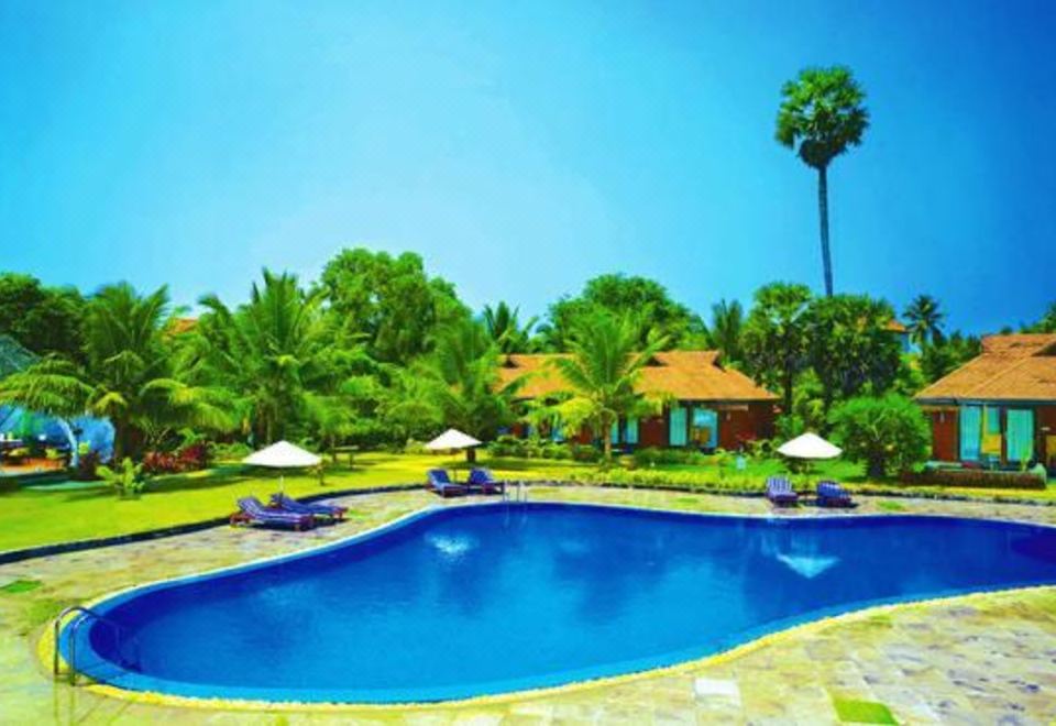 a large blue swimming pool surrounded by lush greenery and palm trees , creating a serene and inviting atmosphere at Poovar Island Resort