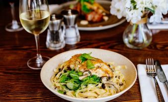 a plate of pasta with shrimp and mushrooms , accompanied by a glass of white wine on a wooden table at The Saracens Head