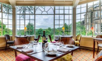 a dining room with a table set for two people , surrounded by windows offering a view of the outdoors at Makeney Hall Hotel
