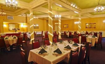 a large , elegant dining room with multiple tables set for a formal dinner , including white tablecloths and red chairs at Hotel Coolidge