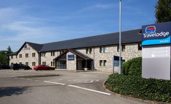 a brick building with a large sign on the front , surrounded by trees and grass at Travelodge Kendal