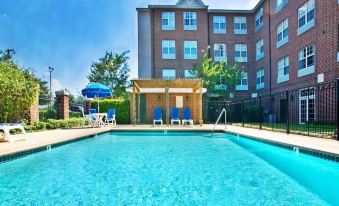 an outdoor swimming pool surrounded by a brick building , with lounge chairs and umbrellas placed around the pool at Holiday Inn & Suites Dallas-Addison