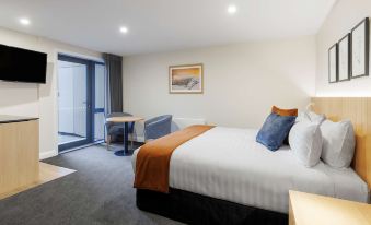 a hotel room with a comfortable bed , a desk , and a door leading to a balcony at Oaks Queenstown Shores Resort