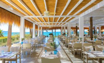 a large dining room with white chairs and tables , blue vases , and a view of the ocean at GrandResort by Leonardo Hotels