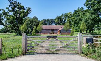 a wooden fence with a gate leading to a house and trees in the background at South Park Farm Barn