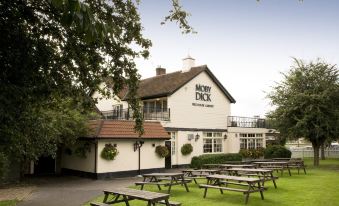 "a white building with a sign that reads "" moby dick "" is surrounded by picnic tables and greenery" at Premier Inn London Romford West
