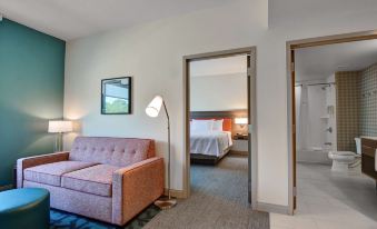 a hotel room with a bed , couch , and lamp , as well as an open door leading to another room at Home2 Suites by Hilton Fort Mill