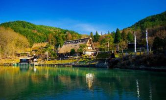 a picturesque lake surrounded by lush green trees , with a small wooden house situated near the water 's edge at Country Hotel Takayama