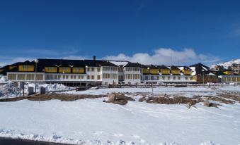 a large , modern building with a long , yellow - colored exterior and white - colored roof is situated on a snow - covered hillside at Luna Hotel Serra da Estrela