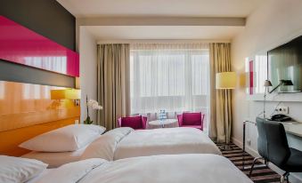 a modern hotel room with white bedding , pink cushions , and a large window offering views of the city at Park Inn by Radisson Katowice