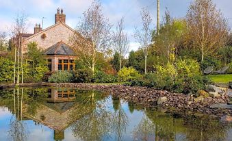 a house is reflected in a pond with trees and bushes , while the sky is partly cloudy at Blackwell House
