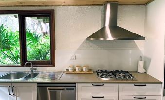 a modern kitchen with white cabinets , a stainless steel range hood , and a large window at William Bay Cottages