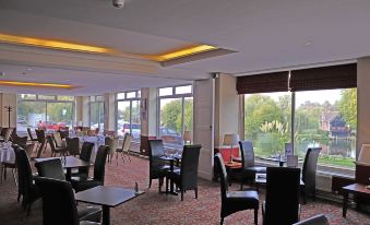 a large , well - lit room with numerous tables and chairs , some of which are occupied by people at Shillingford Bridge Hotel