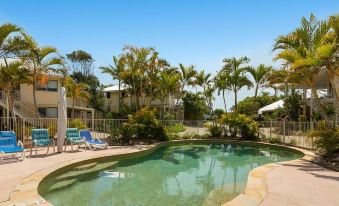a resort with a swimming pool surrounded by palm trees and a blue sky , providing a relaxing atmosphere at Hastings Cove Holiday Apartments
