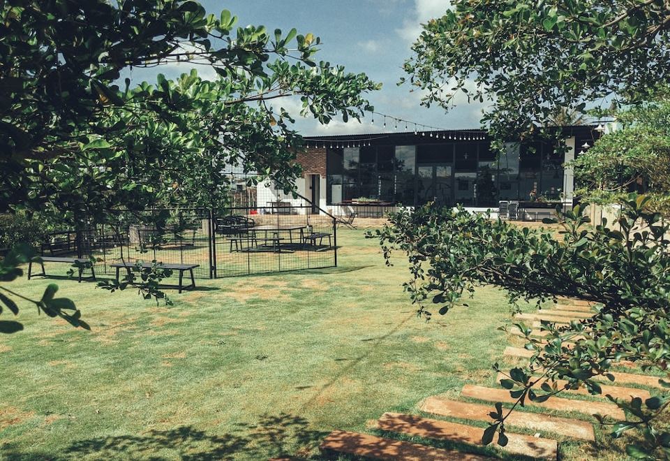 a large , open - air courtyard with a brick building and a metal fence , surrounded by trees at XOM Organic Farm Stay