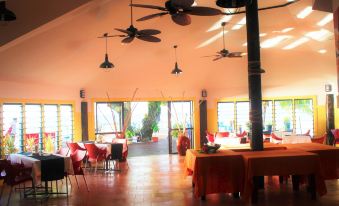 a large dining room with multiple tables and chairs , some of which are occupied by people at Le Uaina Beach Resort