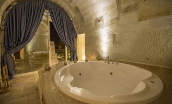 a large white bathtub is situated in a room with stone walls and a blue drape at Azure Cave Suites - Cappadocia