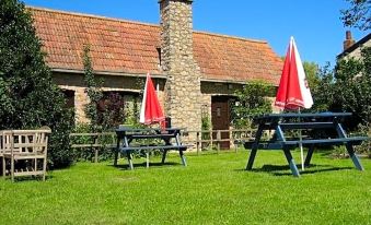 a picnic area with picnic tables and umbrellas , surrounded by a grassy field and a building at The Babbling Brook