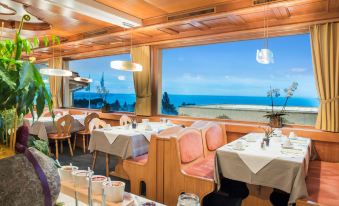 a restaurant with wooden tables and chairs , a window overlooking the ocean , and plates on the table at Best Western Hotel Rebstock