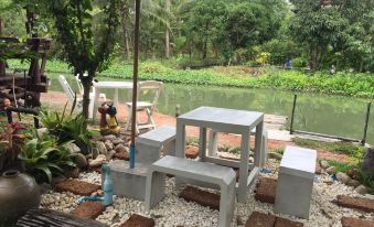 a small outdoor dining area with a table and chairs , surrounded by trees and a pond at BaanSuanLeelawadee Resort Amphawa