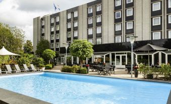 an outdoor pool surrounded by a hotel , with several people enjoying their time in the pool at Novotel Maastricht