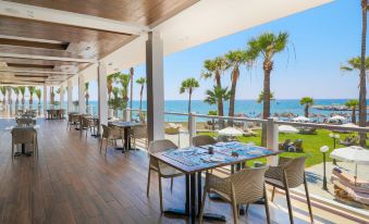 a modern , minimalist restaurant with wooden floors and ceiling , overlooking the ocean , with palm trees in the background at Golden Bay Beach Hotel
