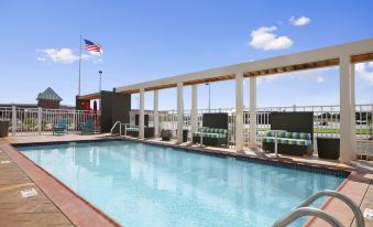 an outdoor swimming pool surrounded by a hotel , with lounge chairs and umbrellas placed around the pool area at Home2 Suites by Hilton Oxford