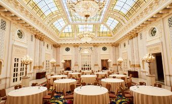 a grand room with white tables and chairs , a large chandelier , and ornate decorations on the walls at Fairmont Grand Hotel - Kyiv