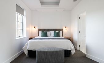 a large bed with white linens and a gray ottoman is in a modern bedroom at The Louise