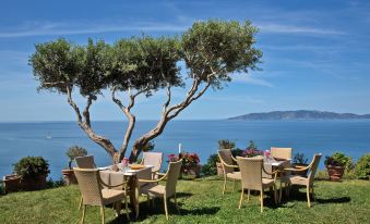 an outdoor dining area with a tree in the foreground and a view of the ocean in the background at Boutique Hotel Torre di Cala Piccola
