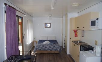 a small , well - furnished bedroom with a bed and a kitchen area in the background at Deniliquin Pioneer Tourist Park
