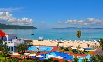 a large pool area with umbrellas and people near the water , overlooking a beach and mountains at Okuma Private Beach & Resort