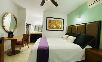 a hotel room with a large bed , a desk , a chair , and a painting on the wall at Cactus Inn Los Cabos