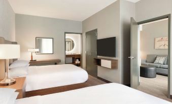 a modern hotel room with two beds , a flat - screen tv , and a bathroom visible through an open door at Embassy Suites by Hilton South Jordan Salt Lake City