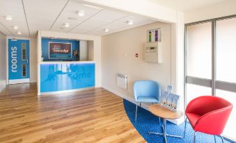 a modern office space with blue walls , wooden floors , and a reception desk , featuring comfortable seating arrangements and a large window at Travelodge Nottingham Trowell M1